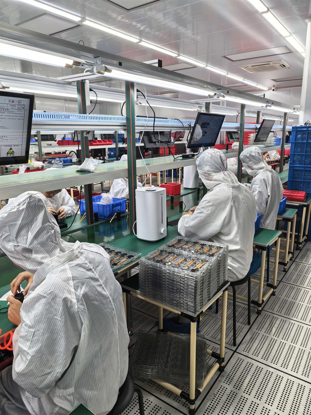 cleanroom assembly line — hooded technicians at green benches